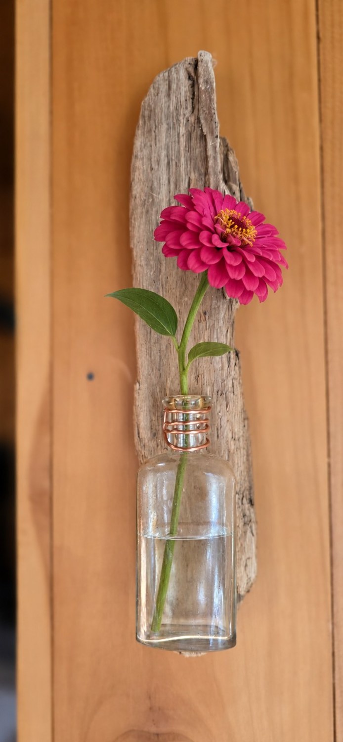 Handmade wood and bottle wall vase with a pink zinnia